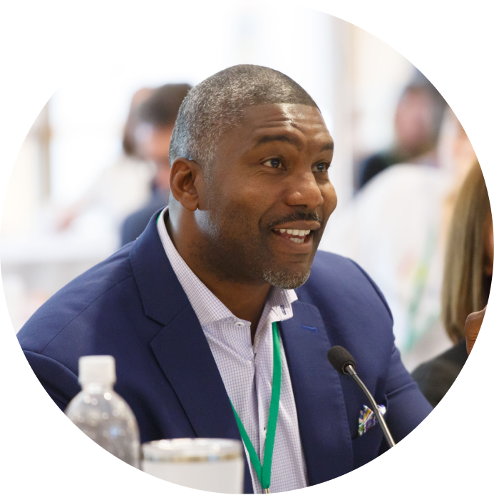 A seated man with a lanyard smiles into a desk microphone