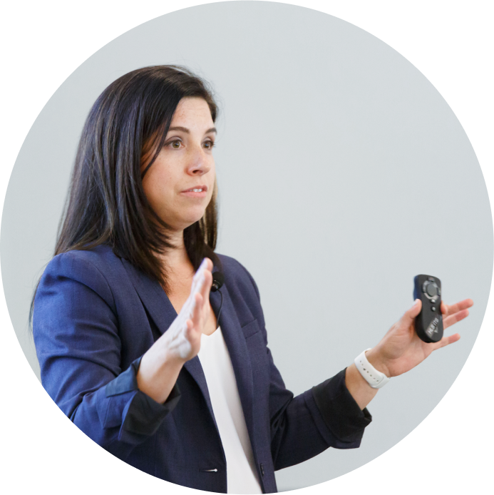 A women speaks on stage, holding a presentation clicker